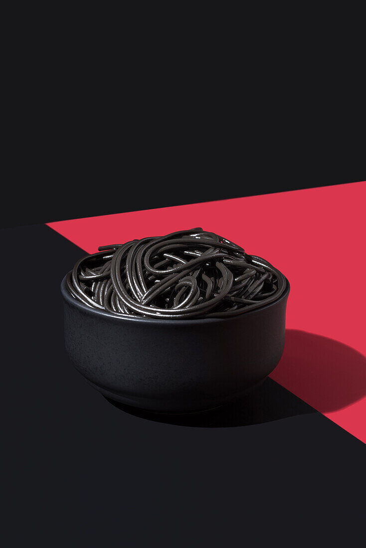 Black spaghetti in a bowl placed on black and red surface against black wall