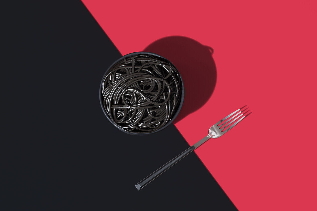 Draufsicht auf schwarze Spaghetti in einer Schüssel auf schwarzem und rotem Hintergrund neben einer Gabel