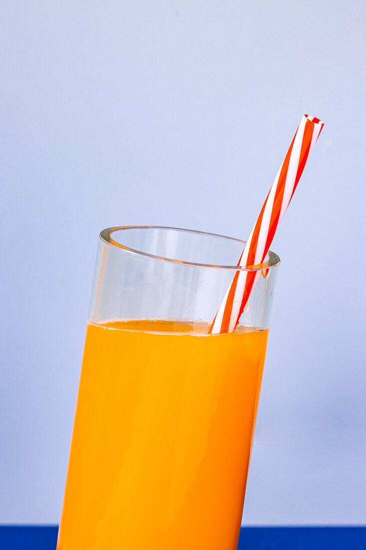 Close up shot of glass of fresh orange juice cocktail with spill on blue background