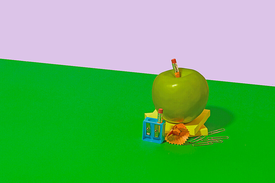Granny Smith apple placed on sticky notes near office or school supplies on bright green and white background