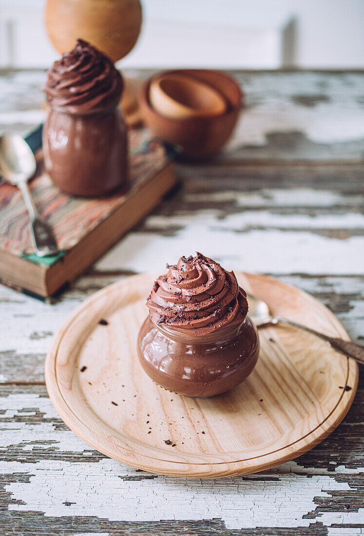 Delicious sweet chocolate mousse desserts in glass jars with silverware on wooden table against white background