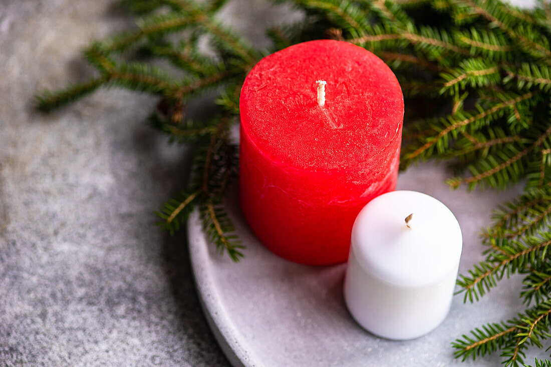 Von oben auf grauer Keramikoberfläche platzierte Kerzen neben grünen Tannenzweigen als Symbol für Weihnachten