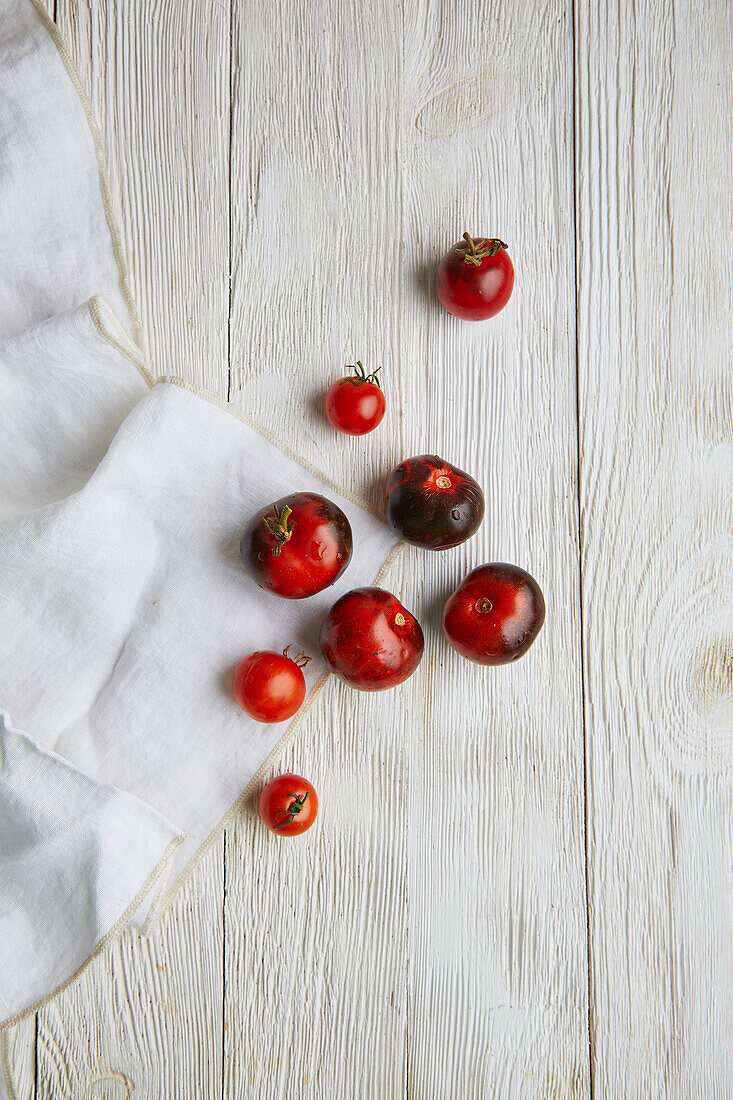 Top view of fresh ripe red cherry tomatoes placed on grey wooden table with white fabric