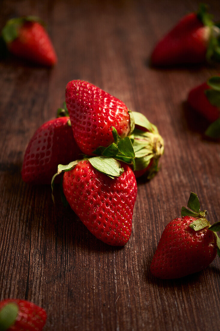 Komposition aus frischen, appetitlichen Erdbeeren mit grünen Blättern, die auf einem Haufen auf einer Holzfläche angeordnet sind