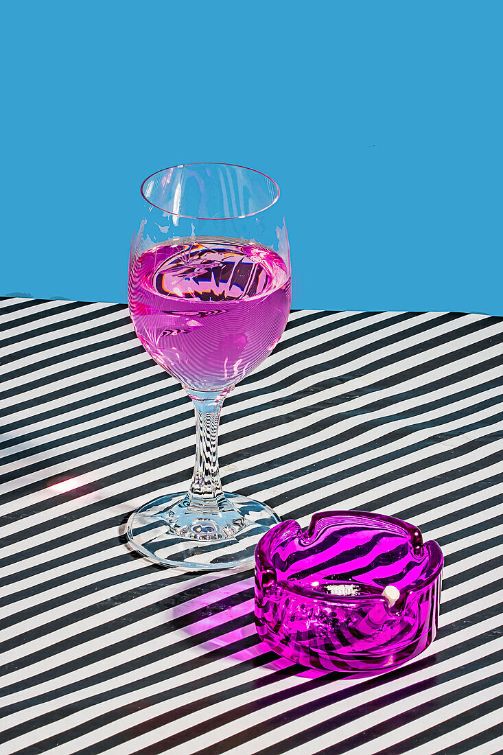 Purple cocktail glass served on a striped fabric surface with a purple ashtray