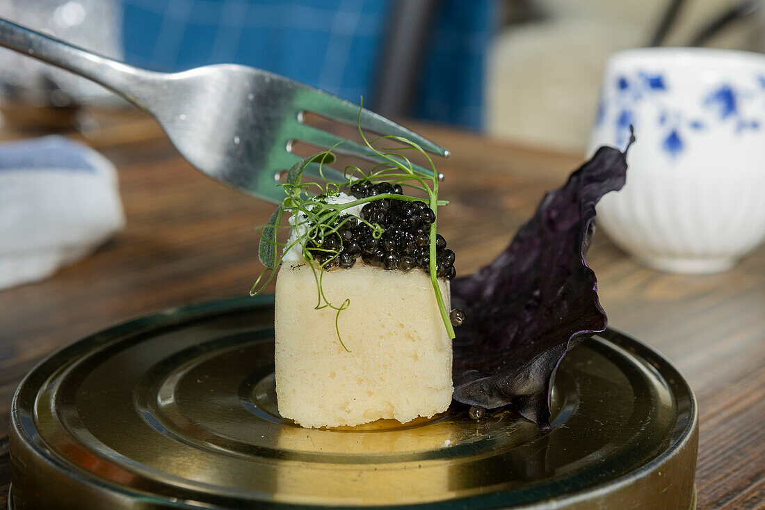 A Michelin star restaurant in Zermatt presents a fusion cuisine masterpiece featuring a delicate cream-based dish topped with luxurious caviar, garnished with a sprig of green and served on elegant metallic tableware.