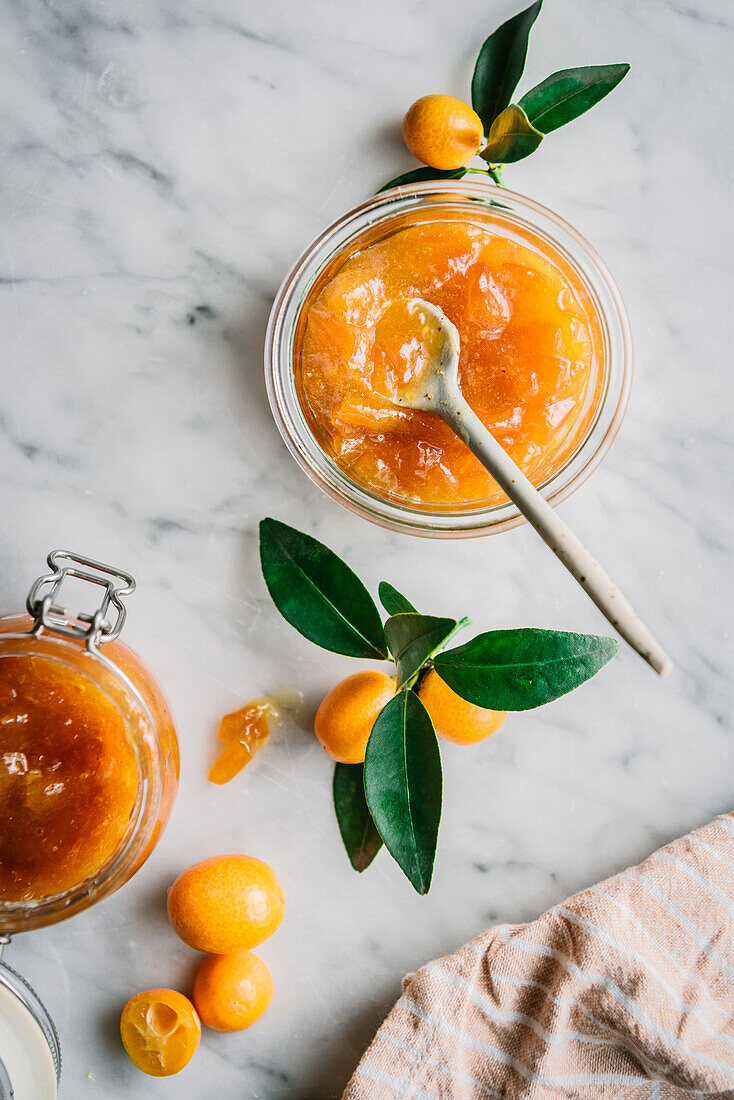 Top view of glass jar with fresh kumquat jam with spoon on table over blur dark grey background