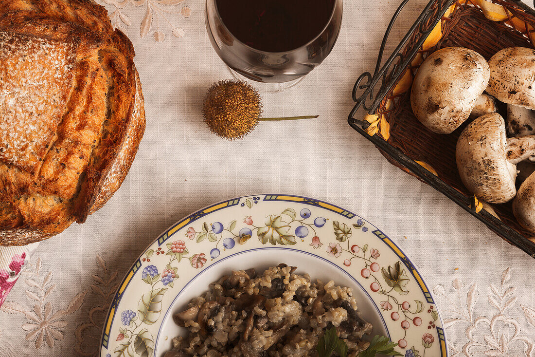 Draufsicht auf eine rustikale Mahlzeit mit traditionellem Pilzrisotto, geschnittenem Brot und einem Glas Wein