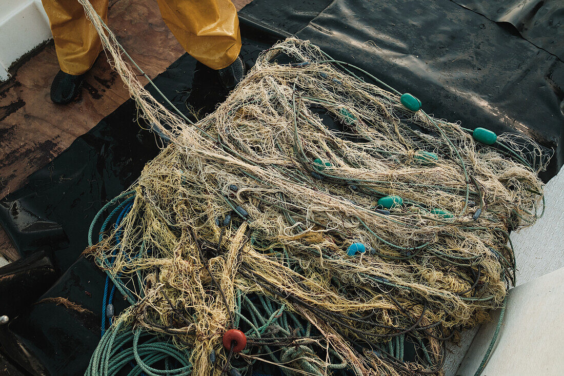 Blick von oben auf ein Fischernetz, das an Deck eines Bootes angebracht ist, und Seile, die bei Tageslicht im Meerwasser von Soller auf Mallorca Spanien befestigt sind, vor verschwommener Natur