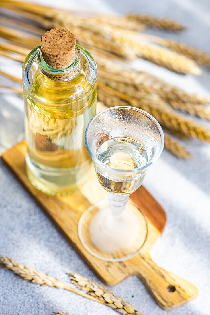 Blick von oben auf ein traditionelles ukrainisches alkoholisches Getränk, das aus Weizen hergestellt wird und als Gorilka bekannt ist, serviert in einem transparenten Glas in der Nähe einer Flasche, die auf einem Schneidebrett steht, vor einem unscharfen Hintergrund