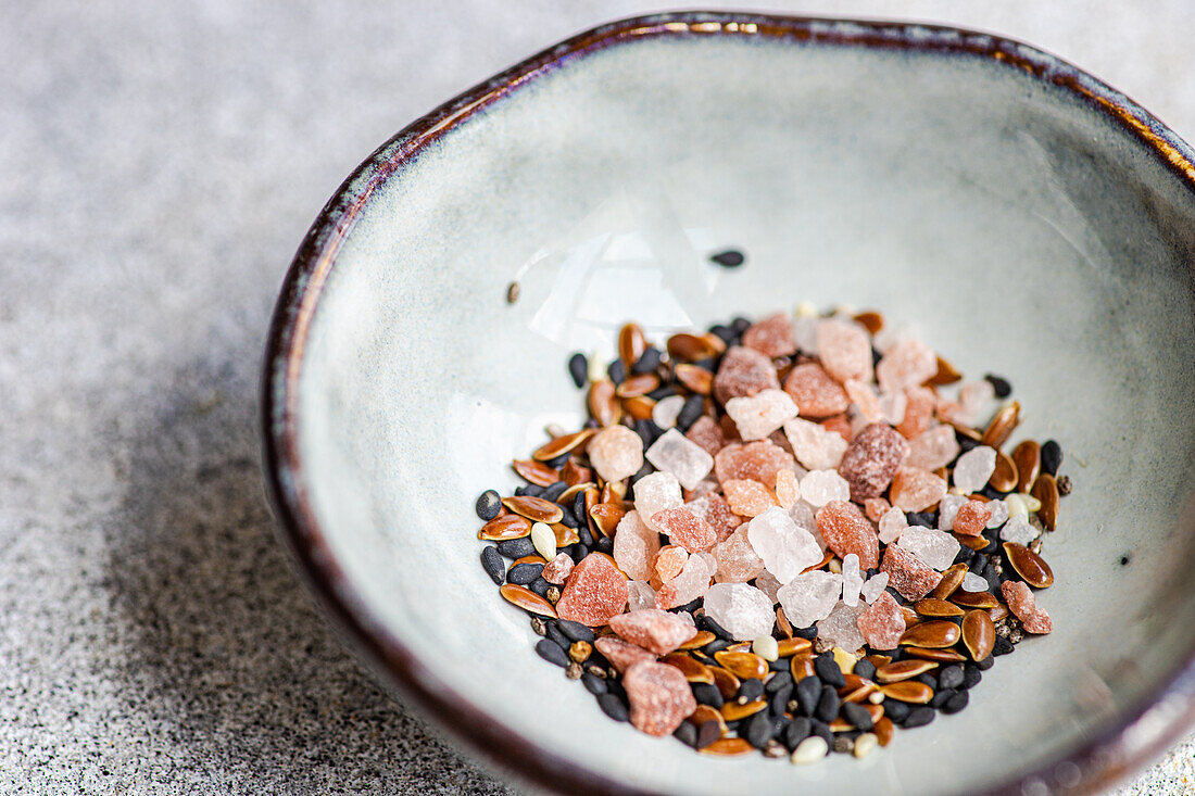 From above of bowl with salad seasoning spices mix consist of Himalayan pink salt, flax seeds, sesame seeds and black pepper on concrete background
