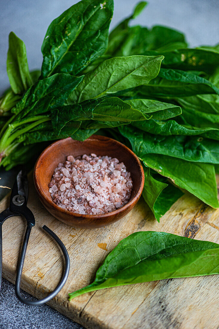 Close up of bunch of fresh spinach leaves on rustic wooden board accompanied by aromatic spices in bowl symbolizing healthy salad preparation