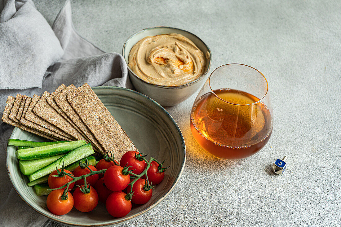 Hoher Winkel eines gesunden Pflanzentellers mit Hummus und Gemüse, serviert in Schalen neben einer Serviette und einem Glas Schnaps vor grauem Hintergrund