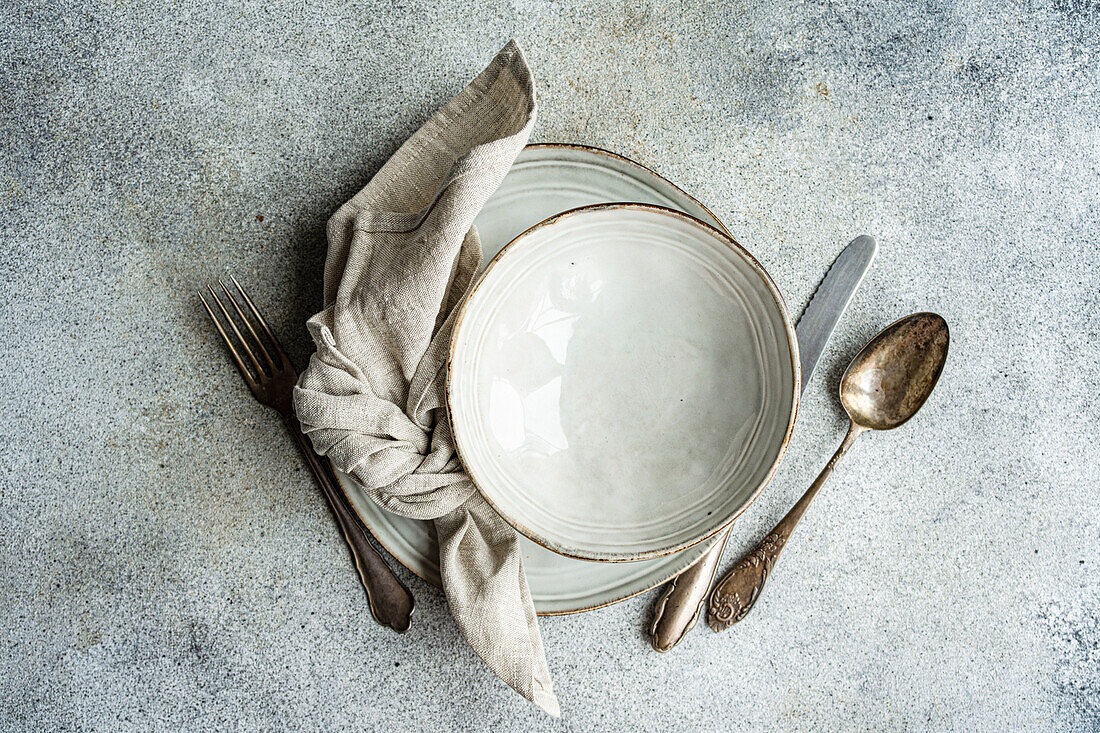Draufsicht auf einen Keramikteller mit Löffel und Serviette neben der Gabel auf einer grauen Fläche am Küchentisch für eine Mahlzeit