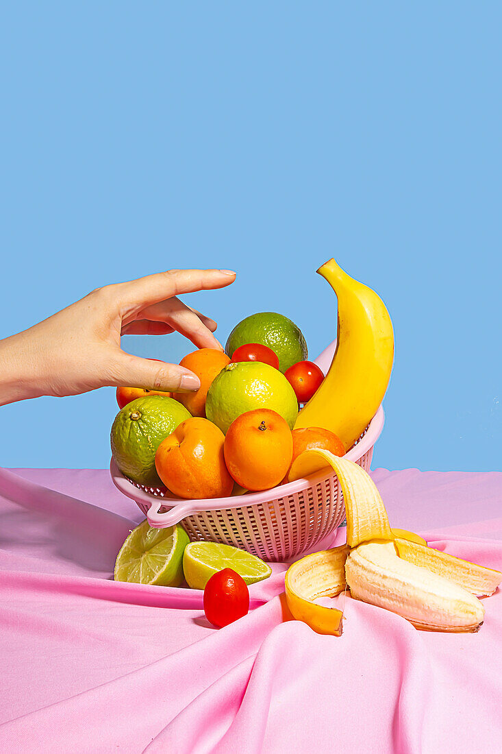 Anonyme Person nimmt einen Pfirsich von einem Plastik-Trockengestell mit frischem Obst auf einem Tisch mit rosa Tischtuch