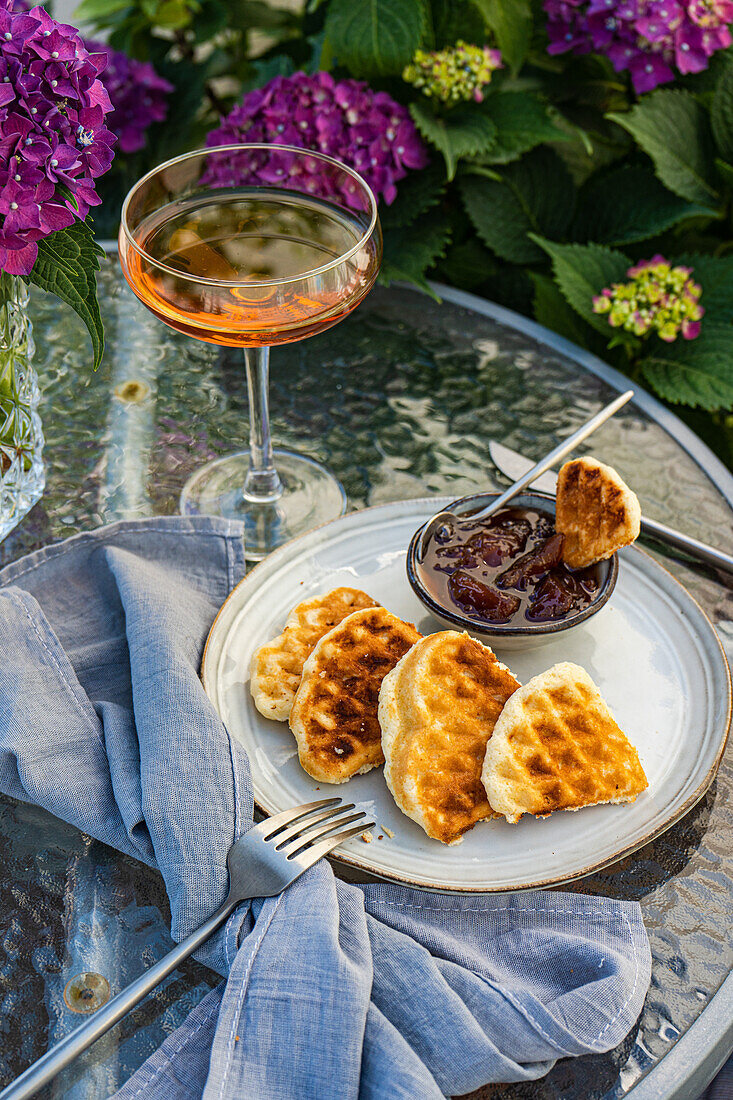 High angle of appetizing sweet waffles served with peach jam on round table near glass with drink in garden with blooming purple Hydrangea flowers