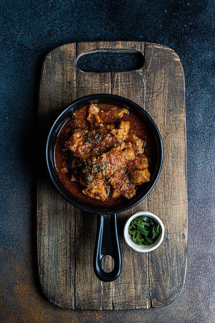 Traditional Georgian dish Ostri served in the frying pan on wooden cutting board