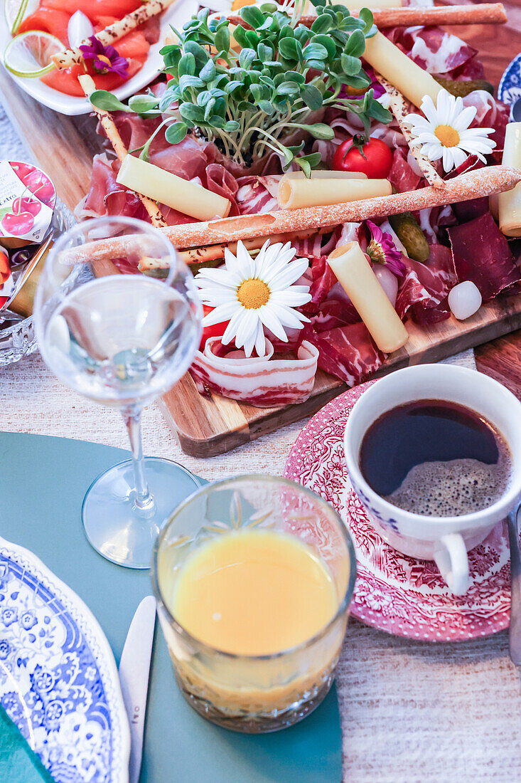 Ein stilvolles Wurstbrett mit verschiedenen Wurstsorten, Käse und frischen Beilagen, begleitet von Wein, frischem Saft und Kaffee