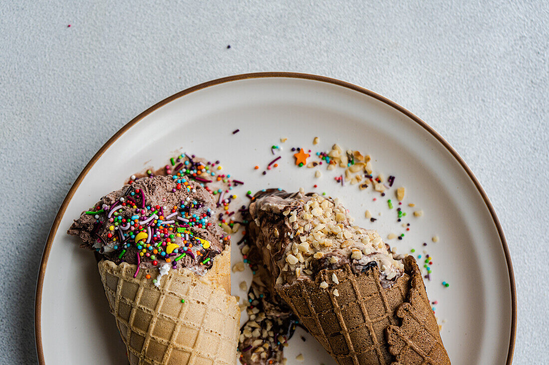 Top view of waffle cones with coffee and chocolate ice cream with multicolored sugar sprinkles and nuts on top in a ceramic dish