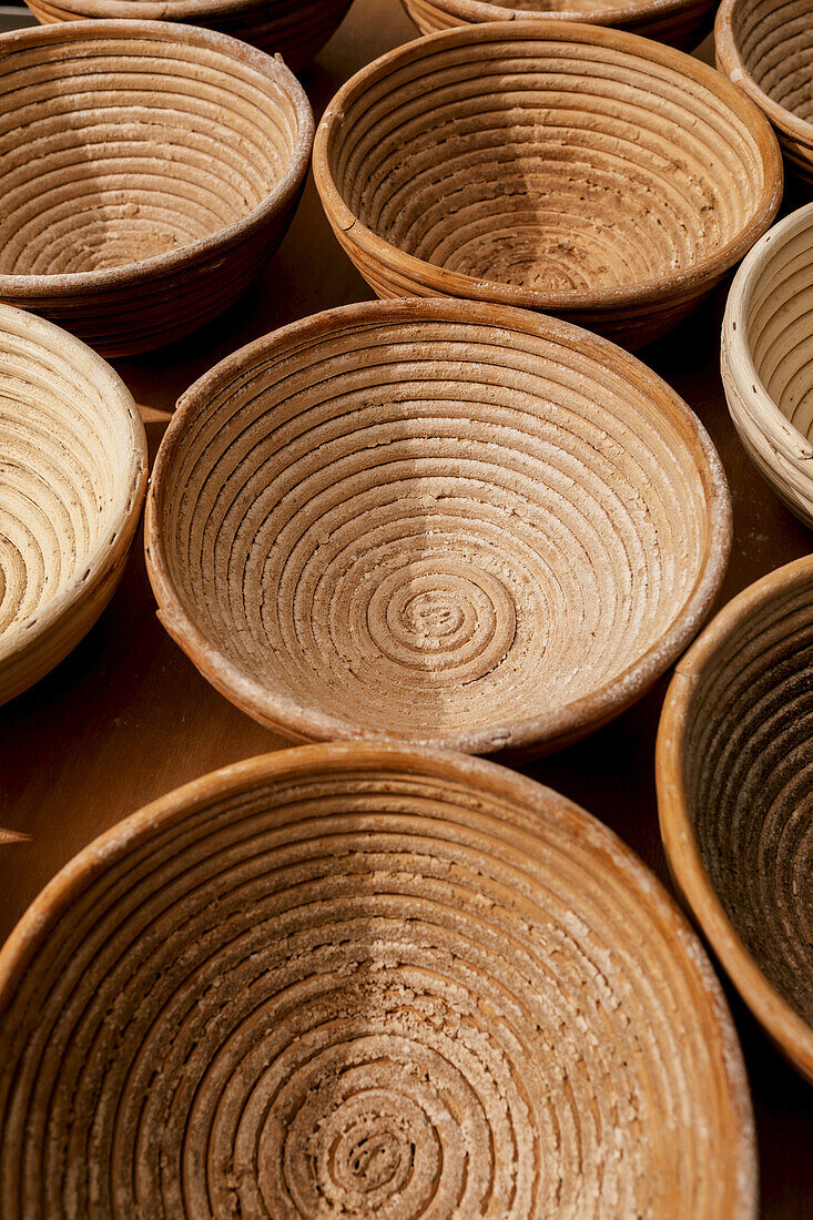 Blick von oben auf braune, runde Gärkörbe aus Holz zum Brotbacken, die auf einem Tisch in der Küche einer Bäckerei stehen
