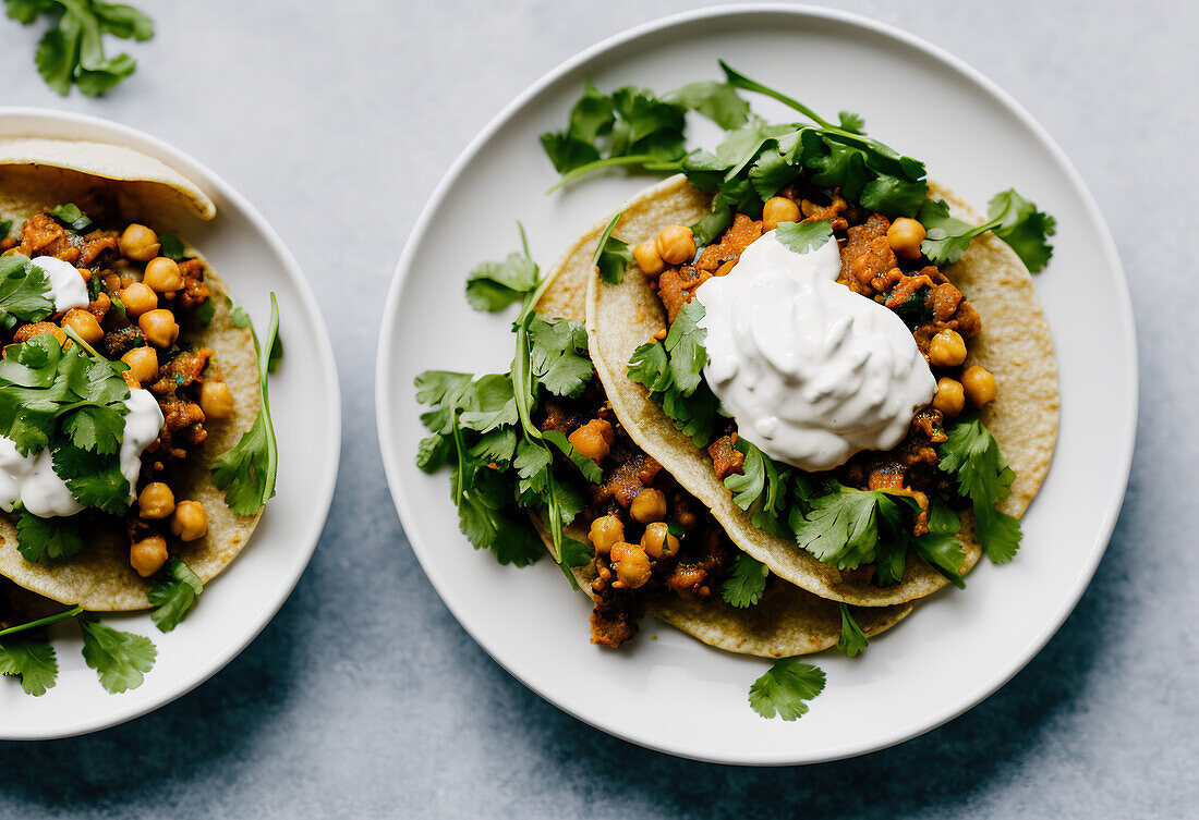 Top view of tasty tortilla flatbread with chickpea and meat topped with cilantro and sour cream served on plates with cutlery over grey table background. Generative AI