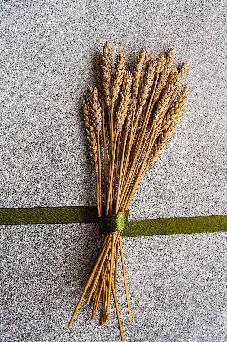 Top view of wheat ears bouquet with green ribbon placed on gray table