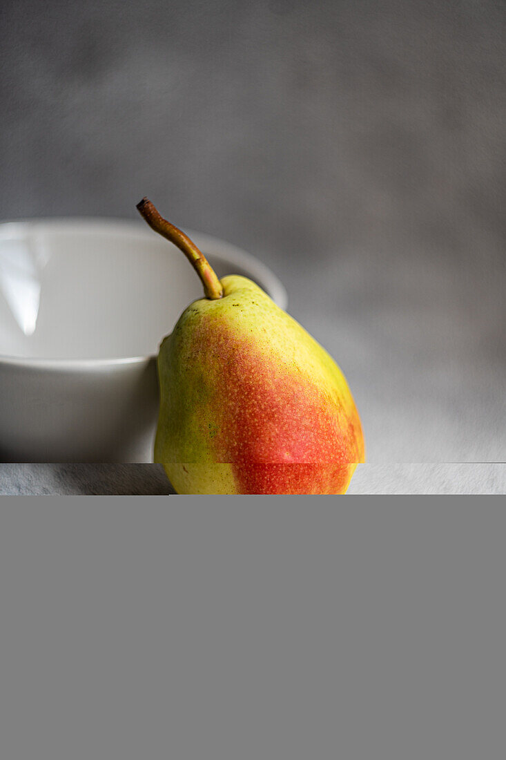 Vorderansicht einer reifen Bio-Birnenfrucht neben einer Schale auf grauem, unscharfem Hintergrund