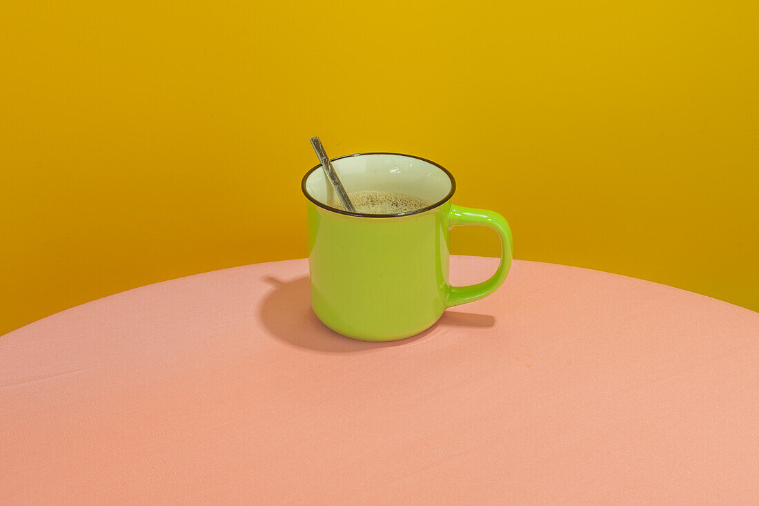 Grüne Tasse mit heißem aromatischem Kaffee und Löffel auf einem runden rosa Tisch vor gelbem Hintergrund