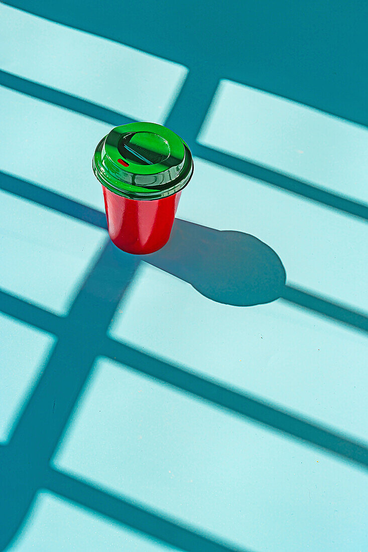 From above of minimalist red plastic cup of takeaway coffee and green lid against blue background