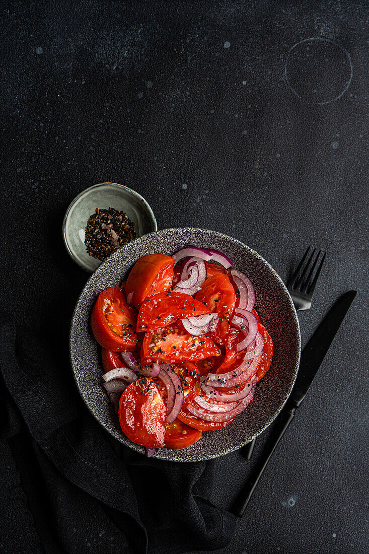 Top view bowl with salad with farm organic tomatoes and red onion with flax seeds and sea salt on black background