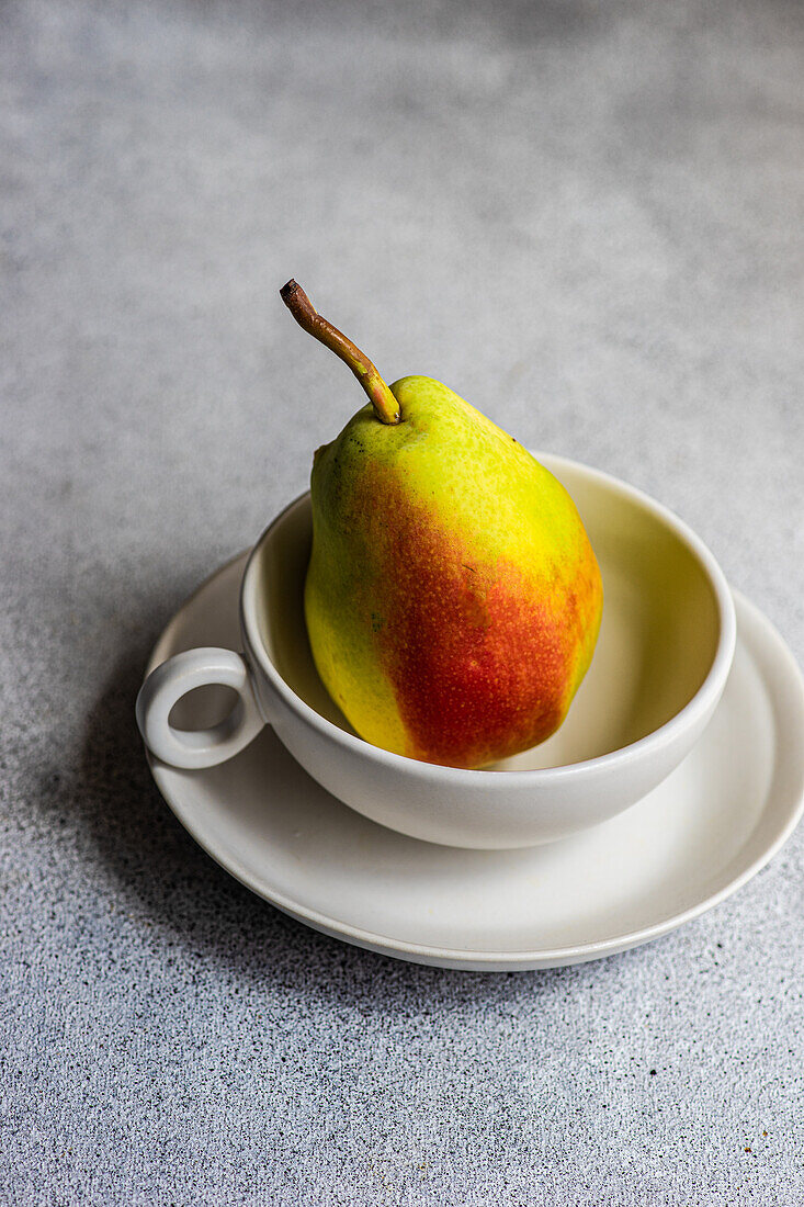High angle of ripe organic pear fruit in cup on plate on gray blurred background