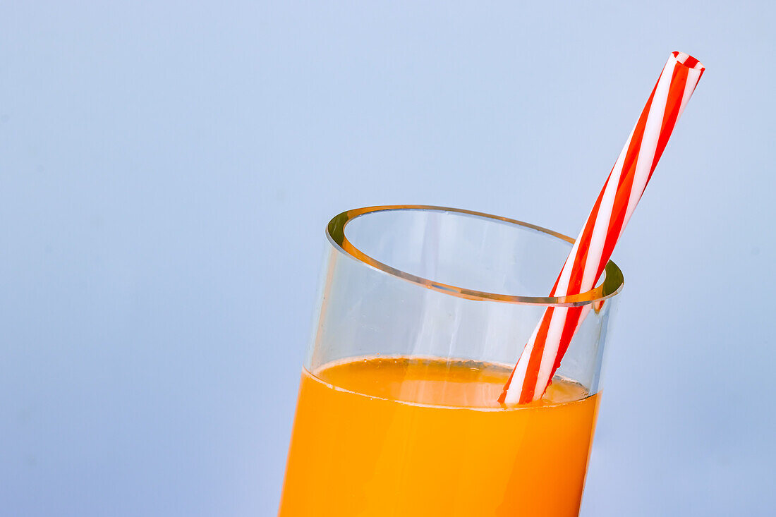 Close up shot of cropped glass of fresh orange juice cocktail on blue background