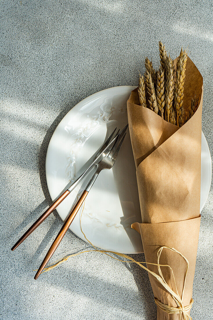 Draufsicht auf einen gedeckten Sommertisch mit Teller, Messer, Gabel und Weizen auf einem grauen Tisch
