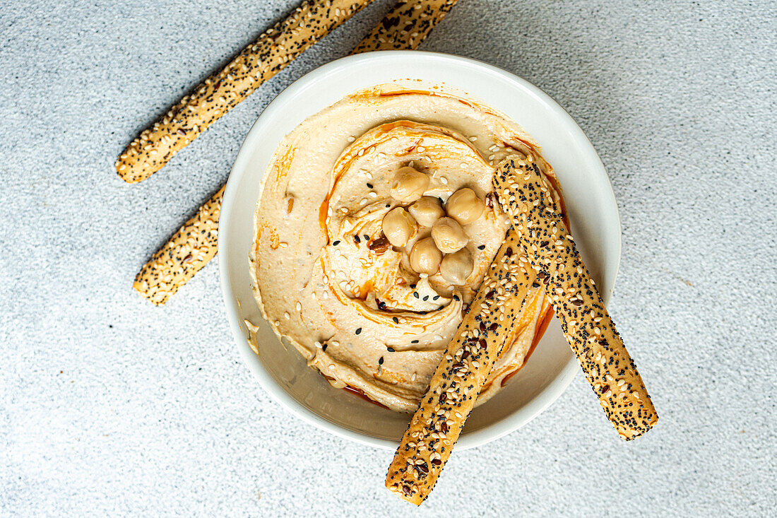 Top view of healthy plant-based plate with hummus and bread sticks served in a bowl against gray background