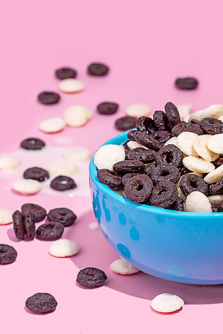 A vibrant bowl filled with chocolate cookies and white baking chips against a pink background, with some scattered around.