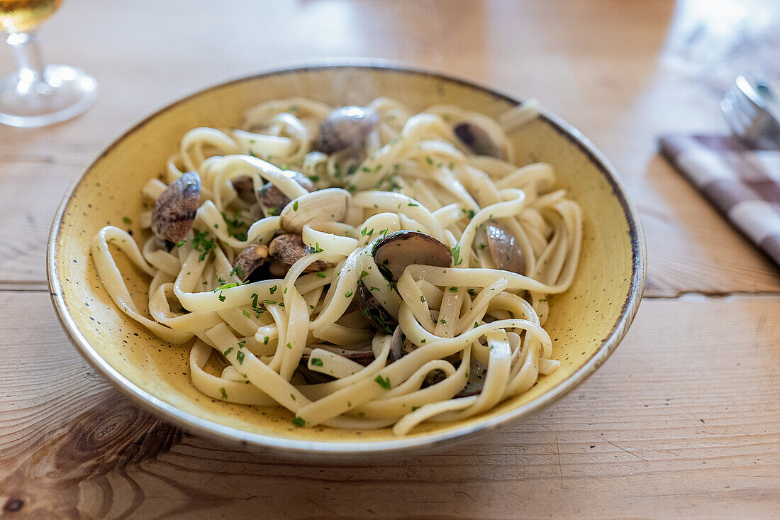 Frisch gekochte köstliche Fettuccine mit Venusmuscheln, serviert in einem Teller mit Besteck und Serviette auf einem Holztisch in einem Restaurant