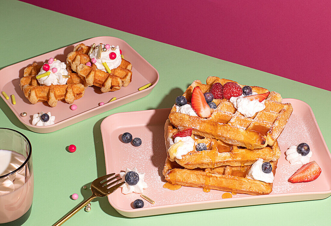 From above tasty sweet waffles topped with berries fruits sauce and cream served on pink tray on colorful table background near glass with hot milk beverage in light kitchen