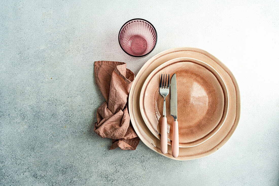 From above sophisticated Easter table setting featuring stacked ceramic plates, rose gold cutlery, and a linen napkin on a textured background.