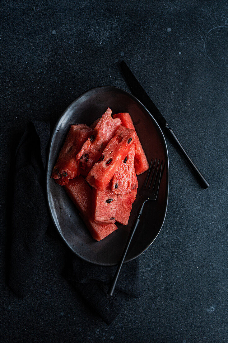 Top view of pieces watermelon on a black plate placed on a dark concrete background
