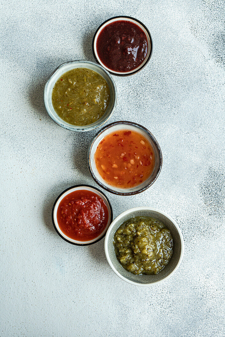 Top view of bowls with traditional Georgian sauces : green plum Tkemali sauce, tomato and cilantro Satsebeli sauce and Kiwi satsebeli placed on white surface