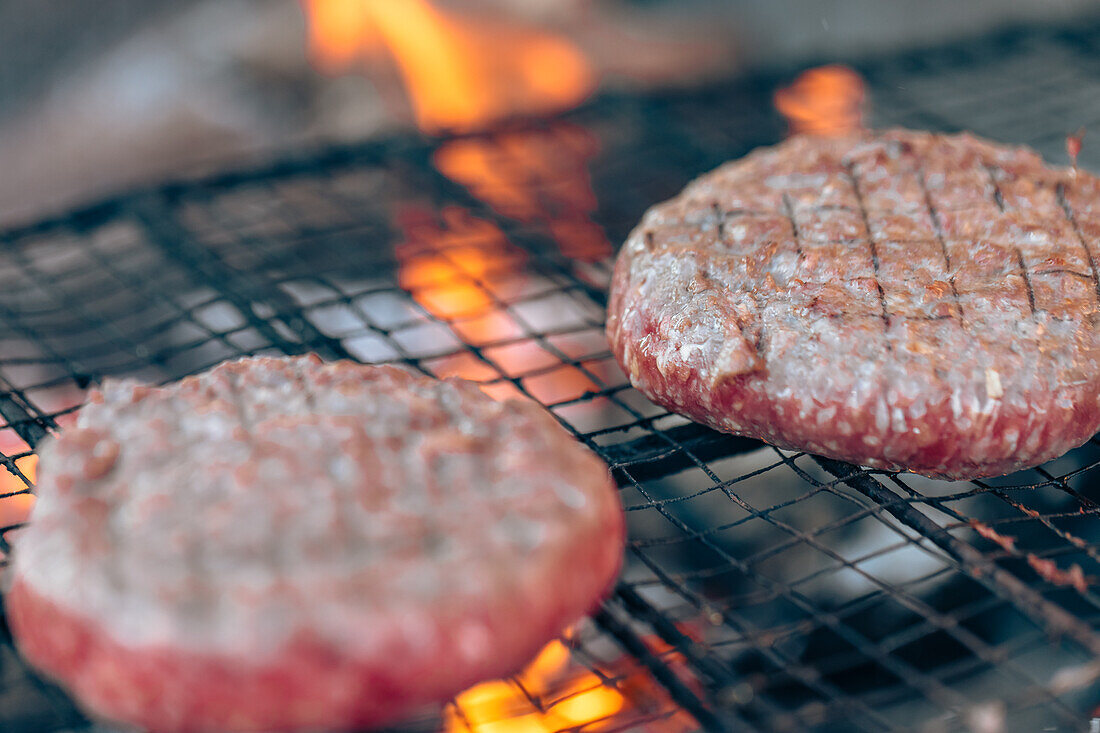 Close-up shot of two burgers cooking on a grill with flames in the background, capturing the essence of a barbecue