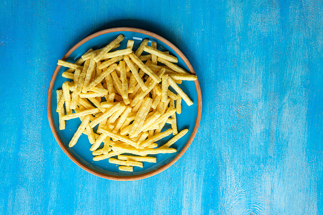 Top view of ceramic plate with French fries placed on blue surface