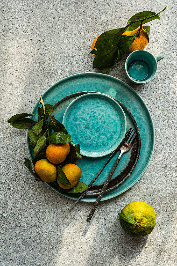 Eine auffällige Komposition mit reifen Mandarinen und Blättern auf einem aquafarbenen Keramikteller, die einen Hauch von natürlicher Frische vermittelt