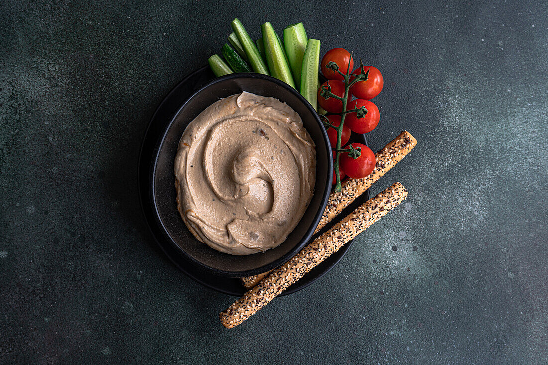 Top view of healthy plant-based plate with hummus and vegetables served in a bowl against gray background