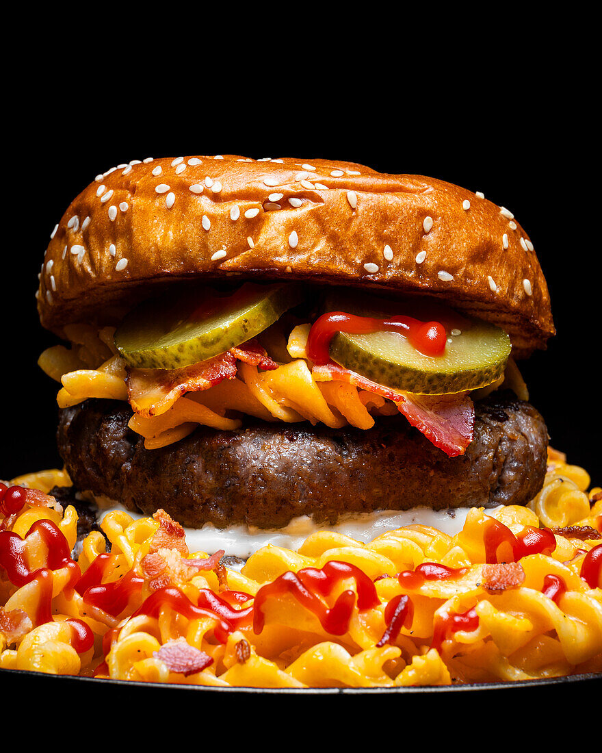 Nahaufnahme eines Hamburgers auf einem Teller mit Makkaroni, Ketchup und Käse vor dunklem Hintergrund