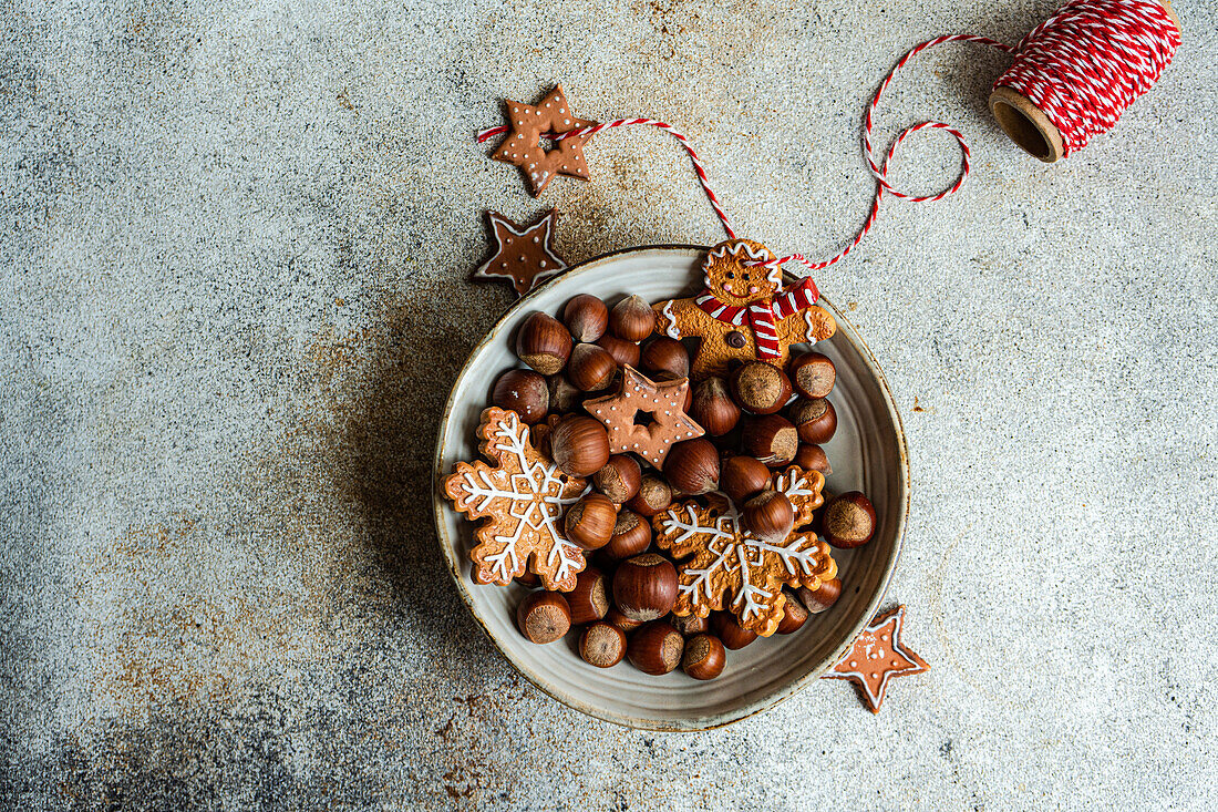 Top view of plate of heap of chestnuts with tasty Christmas cookies placed on table near spool of red thread