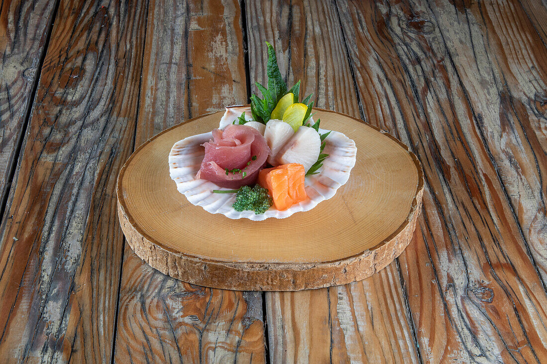 Traditional Japanese sashimi dish with assortment of raw fish served in seashell on wooden background