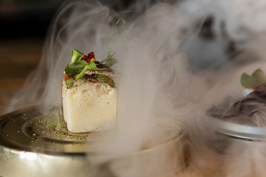 Gourmet fusion dish served with theatrical smoke at a Michelin star restaurant in Zermatt, Switzerland, showcasing local and seasonal ingredients.