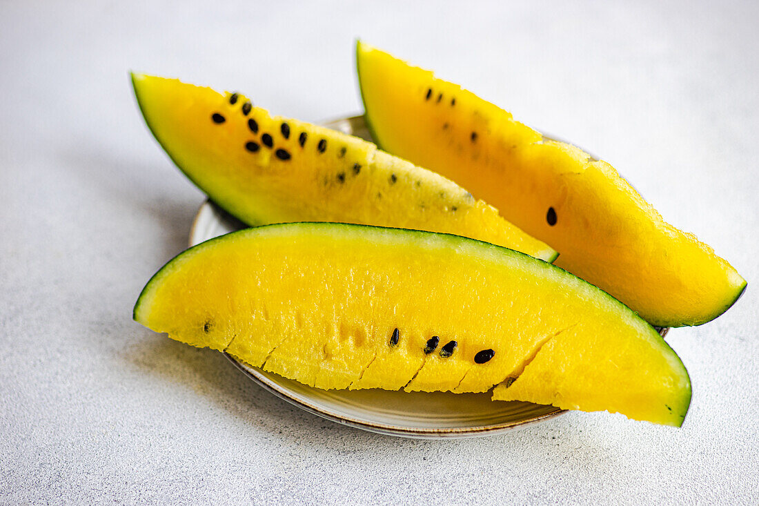 High angle of slices of organic yellow watermelon served on ceramic plate against gray surface