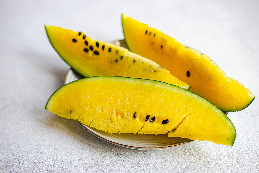 Hoher Winkel von Scheiben organischer gelber Wassermelone, die auf einem Keramikteller vor einer grauen Fläche serviert werden